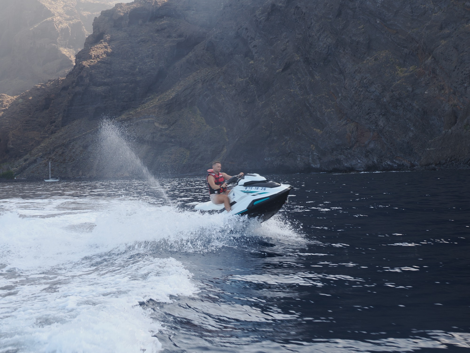 Jet ski carving a wall of spray beneath the cliffs on the Costa Adeje coastline